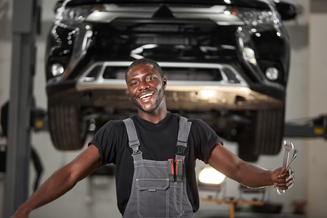 Smiling technician standing beneath an SUV raised on a workshop lift